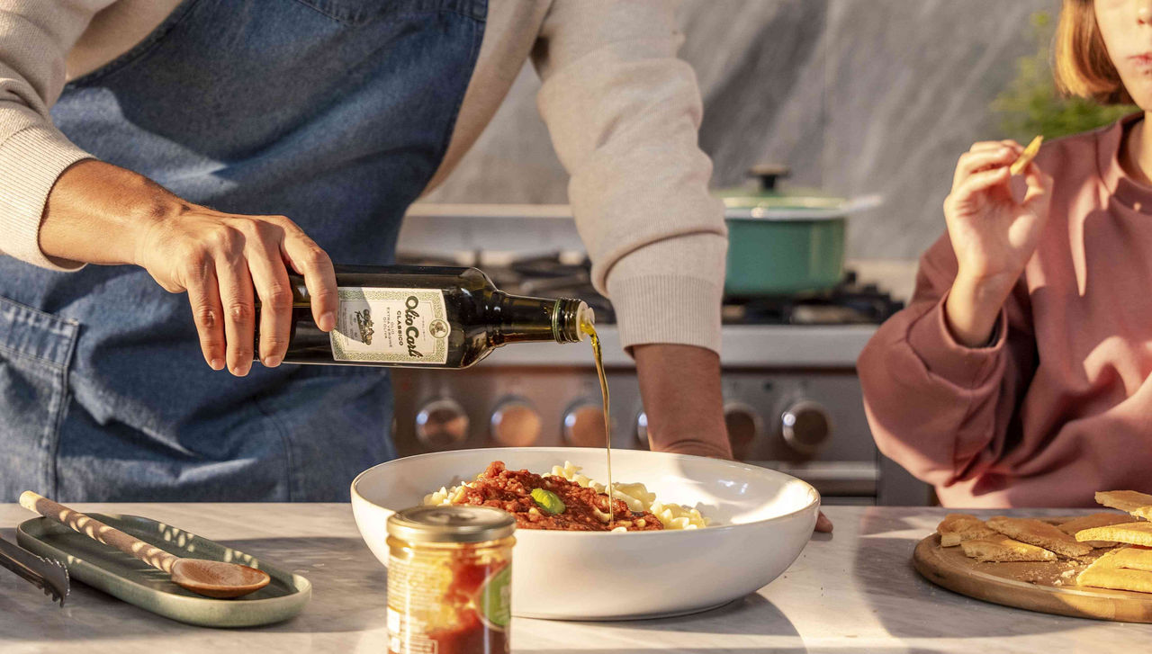 Vater und Tochter am Tisch vollenden Pasta mit Sauce mit einem Schuss Carli Nativem Olivenöl Extra Classico