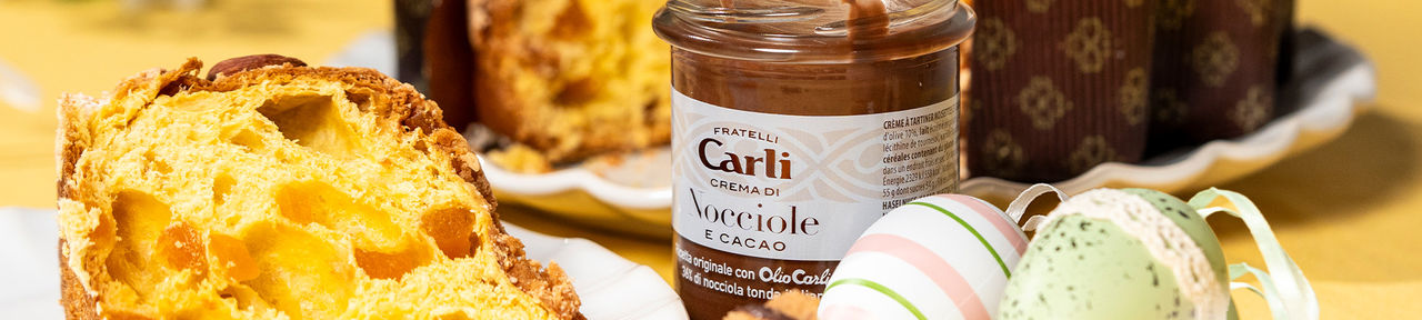 Tranche de gâteau Colomba accompagnée d’un pot de crème de noisettes et de petits œufs de Pâques colorés.